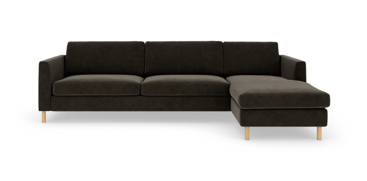 Mørkegrå hjørnesofa med chaiselong til højre og lyse træben, fotograferet lige forfra på hvid baggrund.