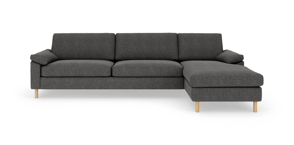 Mørkegrå sofa med chaiselong til højre og lyse træben, isoleret på hvid baggrund.