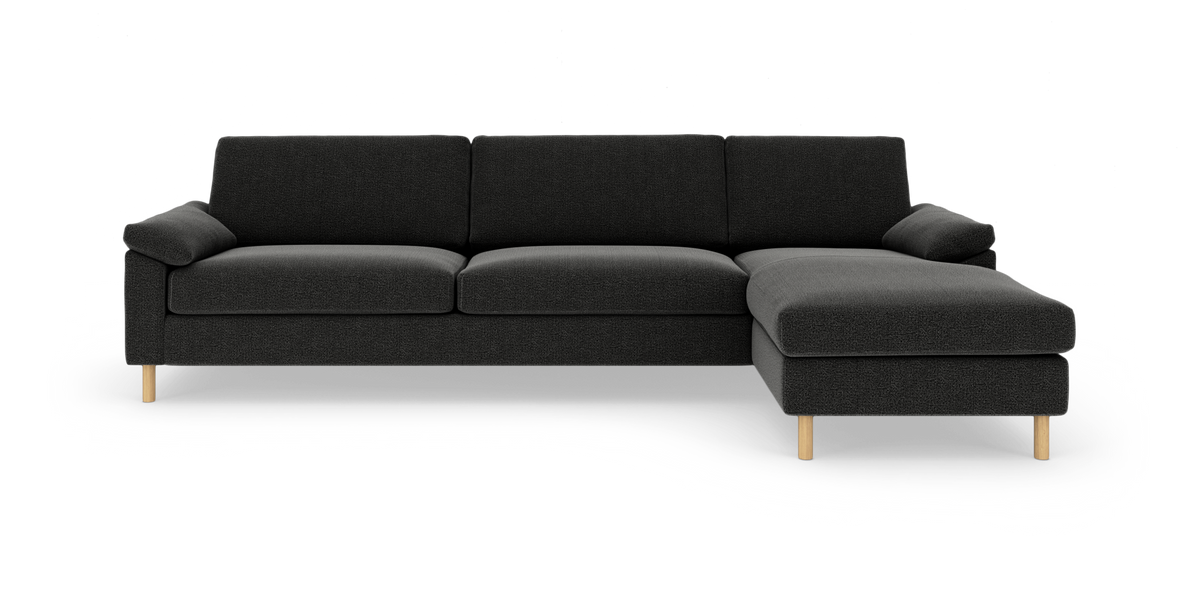 Mørkegrå hjørnesofa med chaiselong til højre og lyse træben, frilagt på hvid baggrund.