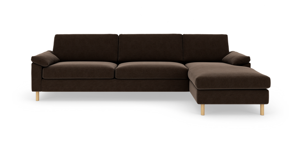 Mørkebrun hjørnesofa med chaiselong til højre og lyse træben, fritlagt på hvid baggrund.