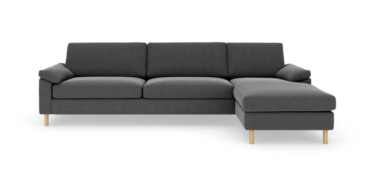 Mørkegrå hjørnesofa med chaiselong til højre og lyse træben, frilagt på hvid baggrund.