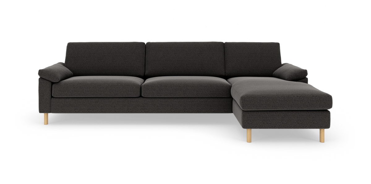 Mørkegrå hjørnesofa med chaiselong til højre på lys baggrund.