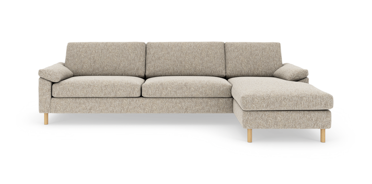 Beige 3-personers sofa med højrevendt chaiselong, stofbetrukket med træben samt løse ryg- og sidepuder.