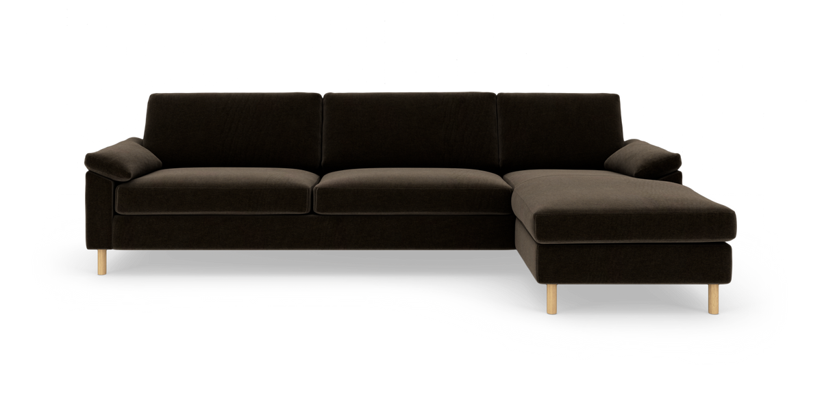 Mørkebrun hjørnesofa med chaiselong til højre og lyse træben, frilagt på hvid baggrund.