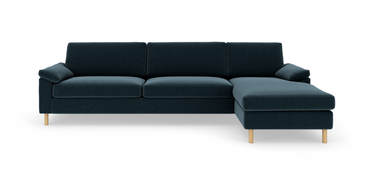 Mørkeblå hjørnesofa med chaiselong til højre og lyse træben, fritlagt på hvid baggrund.