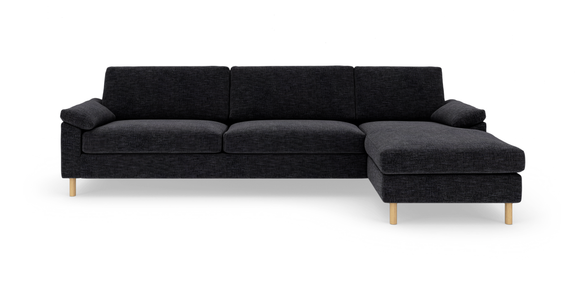Mørkegrå hjørnesofa med chaiselong til højre og lyse træben, frilagt på hvid baggrund.