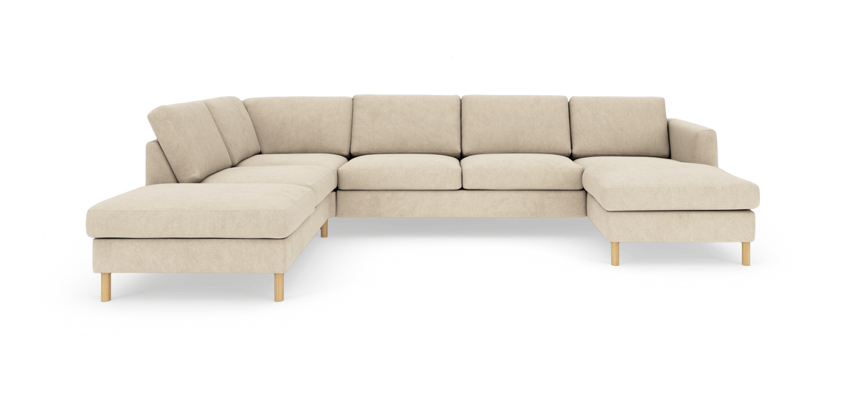 Beige L-formet modulsofa med chaiselonger i begge ender og slanke træben, fritstående mod hvid baggrund.