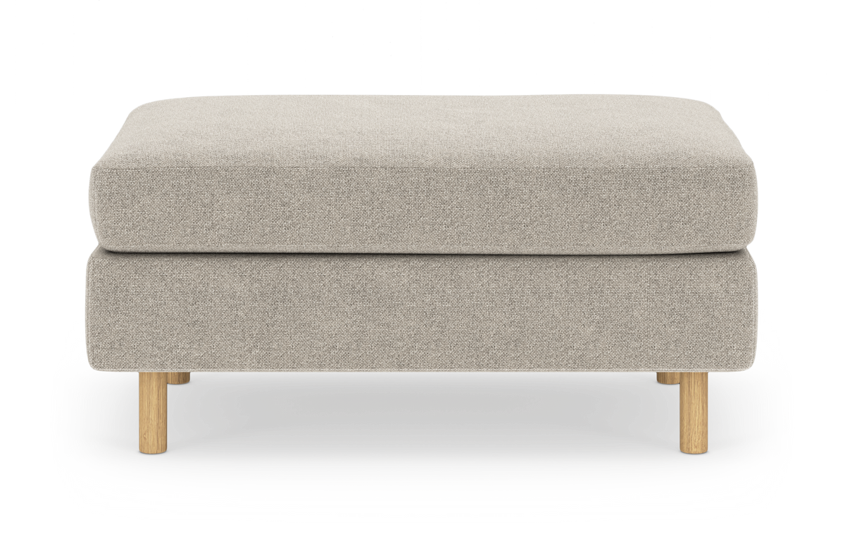 Beige puf/ottoman med afrundede hjørner og lyse træben, set forfra mod hvid studiobaggrund.