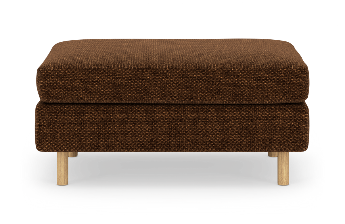 Brun stofpuf/ottoman med lyse træben, frilagt på hvid baggrund.