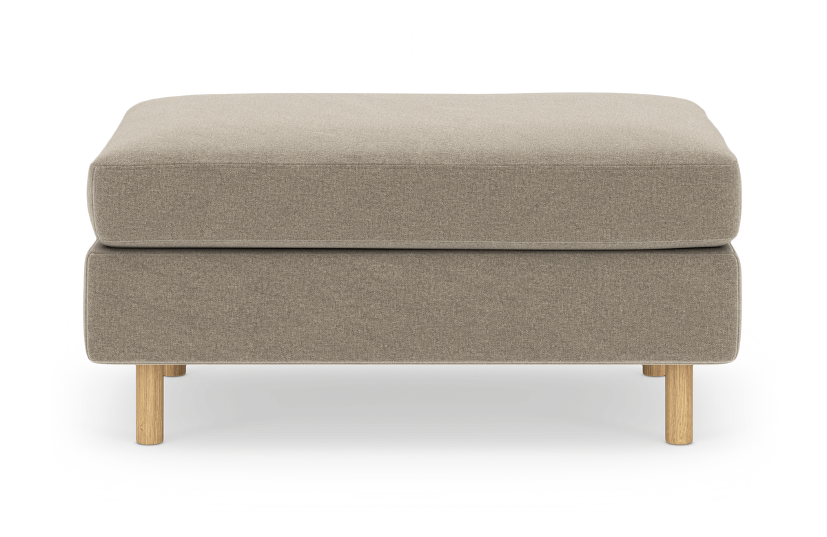 Beige ottoman/fodskammel med runde træben i enkel, moderne udførelse, frilagt på hvid baggrund.