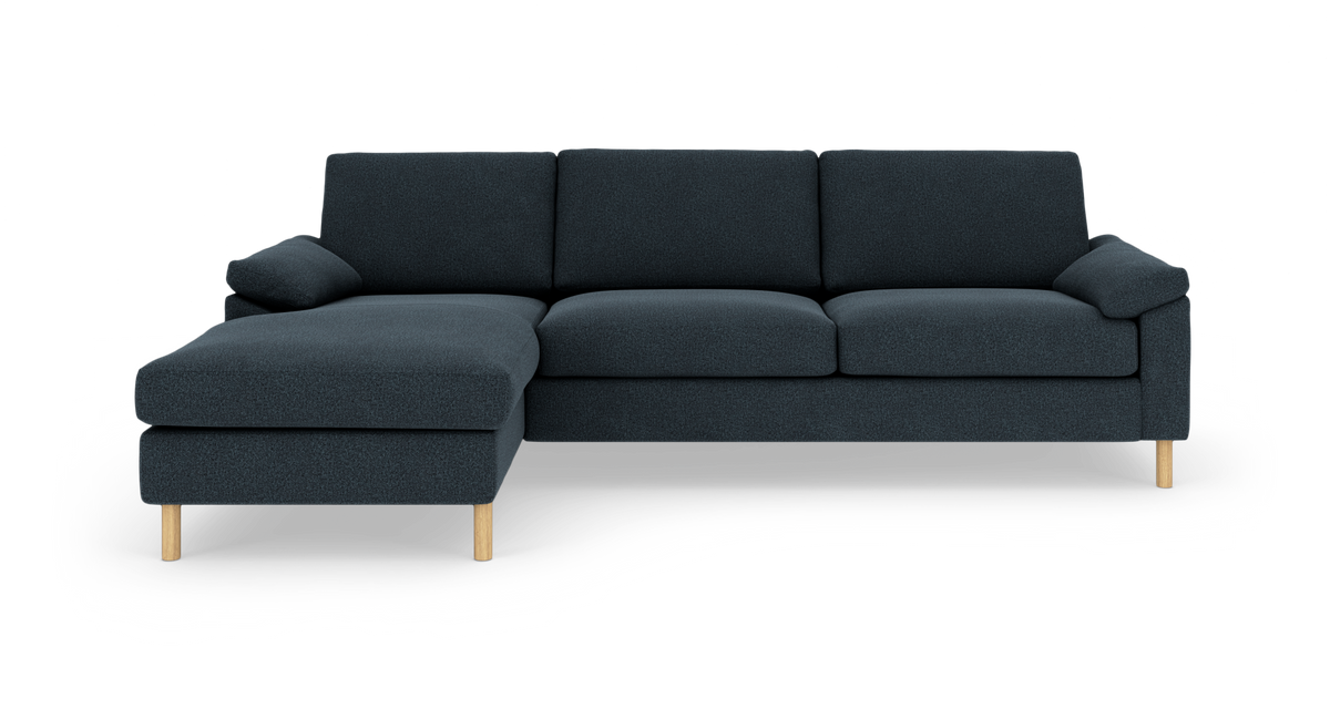 Mørkeblå L-formet hjørnesofa med venstrevendt chaiselong og lyse træben, vist lige for i studiemiljø.
