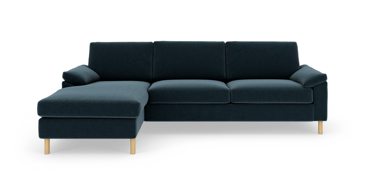 Mørkeblå tresæders sofa med venstrevendt chaiselong og lyse træben, frilagt på hvid baggrund.