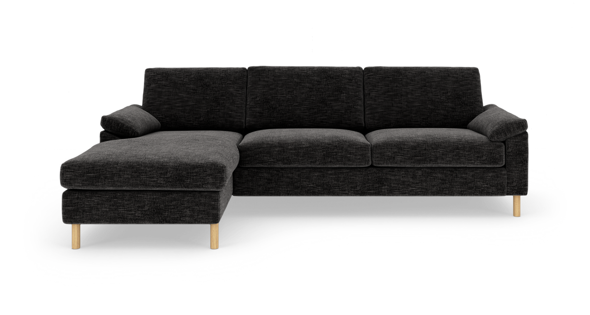 Mørkegrå hjørnesofa med chaiselong til venstre og lyse træben, frilagt på hvid baggrund.