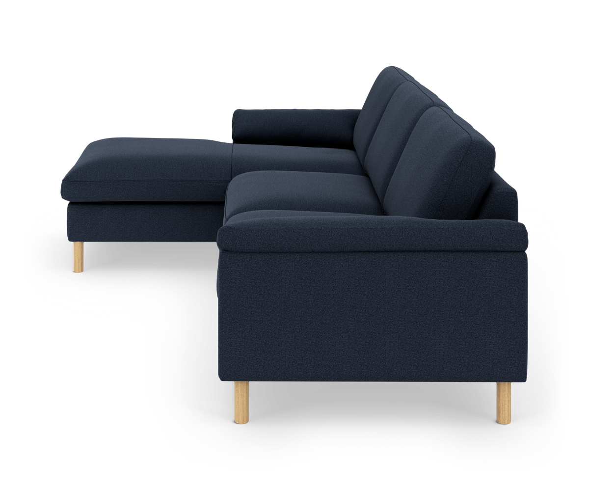 Mørkeblå hjørnesofa med chaiselong og lyse træben, set fra siden på hvid baggrund.
