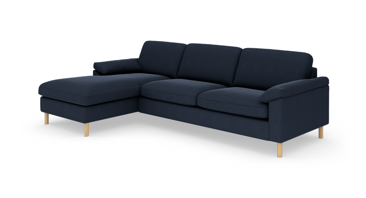 Mørkeblå hjørnesofa med chaiselong til venstre og lyse træben, fritlagt på hvid baggrund.