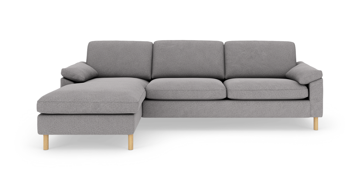 Grå hjørnesofa med venstrevendt chaiselong, stofpolstret og med runde træben, frilagt mod hvid baggrund set forfra.