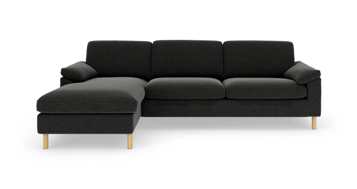 Mørkegrå hjørnesofa med venstrevendt chaiselong, polstrede sæder og lyse træben, frilagt på hvid baggrund.