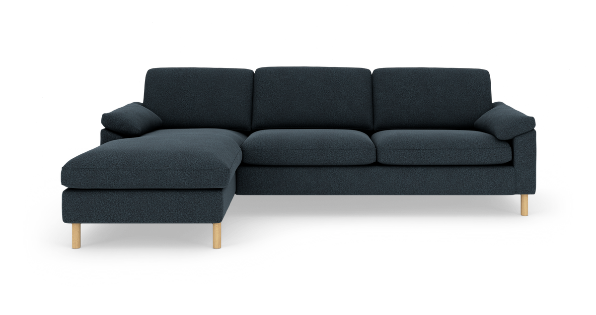 Mørkeblå hjørnesofa med venstrevendt chaiselong og lyse træben, frilagt på hvid baggrund.