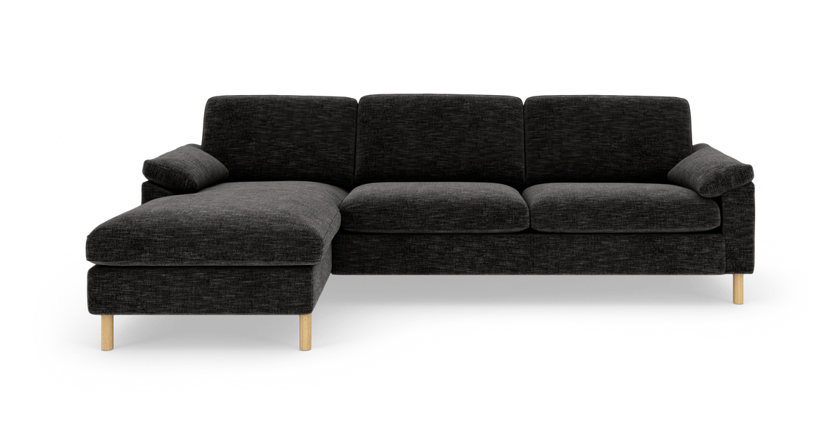 Mørkegrå hjørnesofa med venstrevendt chaiselong, stofbetræk og lyse træben, frilagt på hvid baggrund.