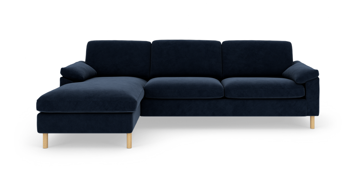 Mørkeblå hjørnesofa med venstre chaiselong og lyse træben, frilagt på hvid baggrund.
