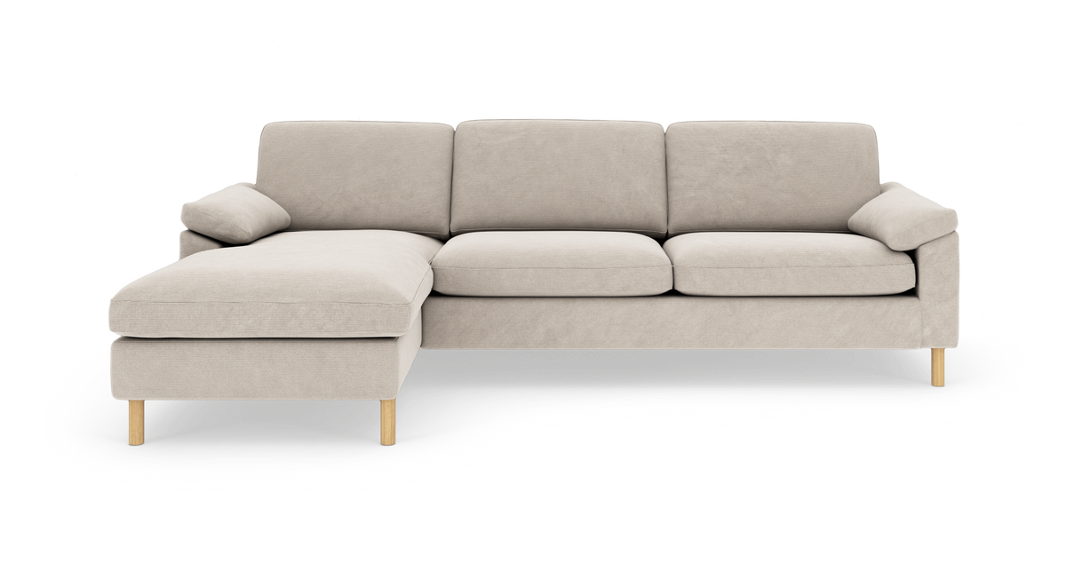 Beige hjørnesofa med venstrevendt chaiselong, stofbetrukket med træben, frilagt på hvid baggrund.