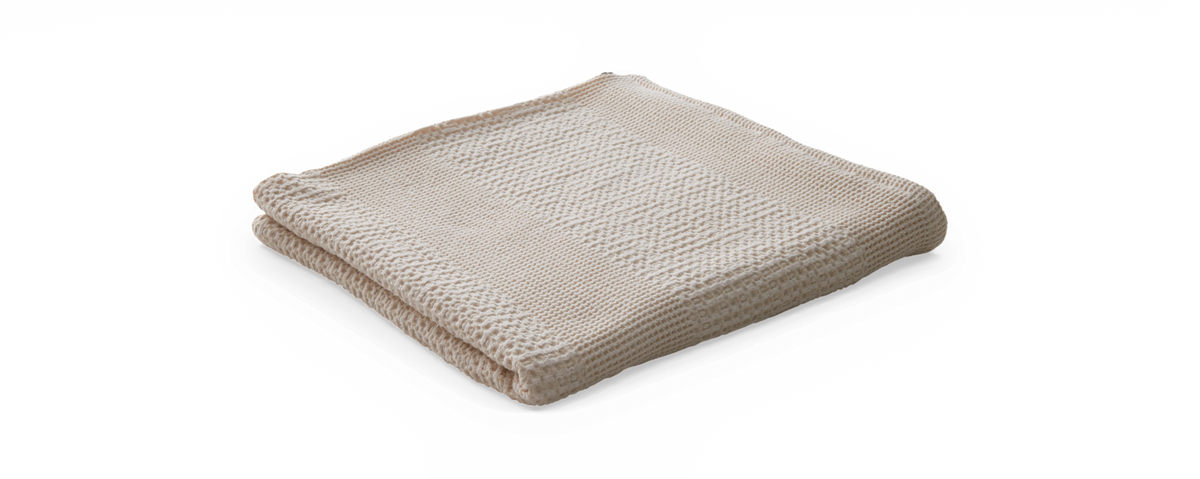Sammenfoldet beige strikket plaid med tekstureret vaffelmønster, frilagt.