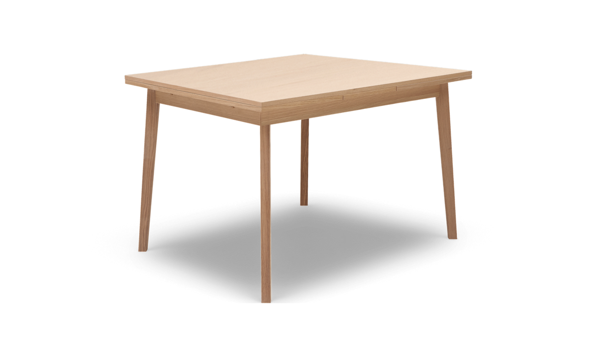 Rektangulært spisebord i lys eg med slanke, tilspidsede ben, set skråt forfra.