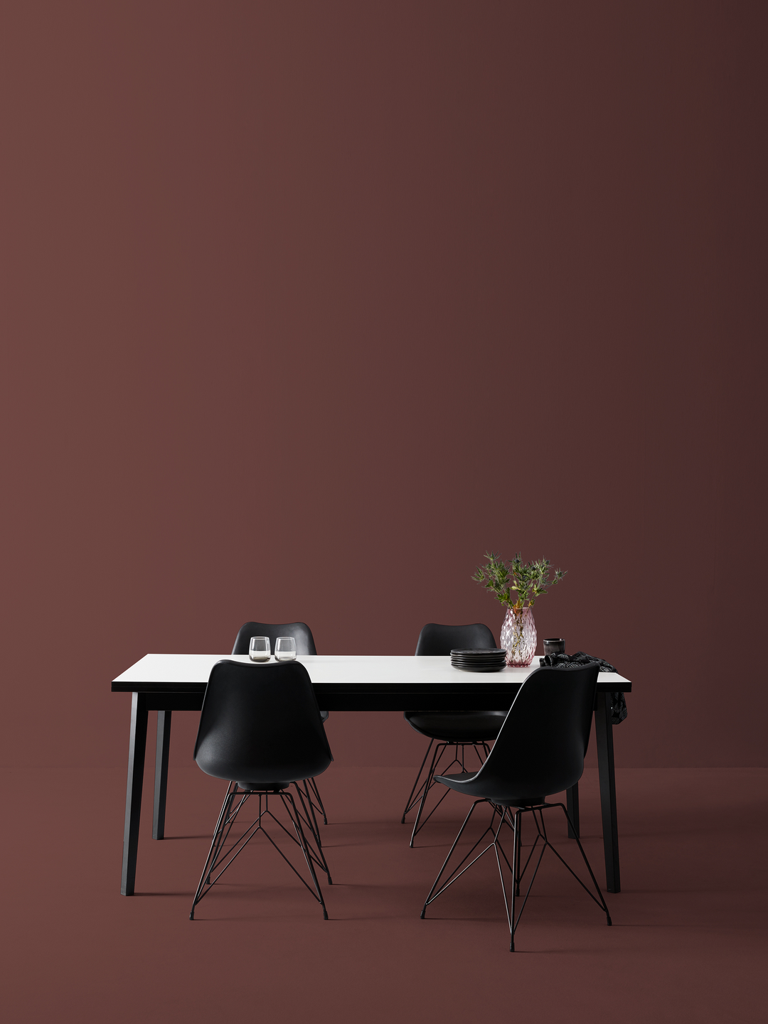 Sort spisebord med hvid bordplade og fire sorte stole; to glas, sorte tallerkener og en vase med grønne kviste.