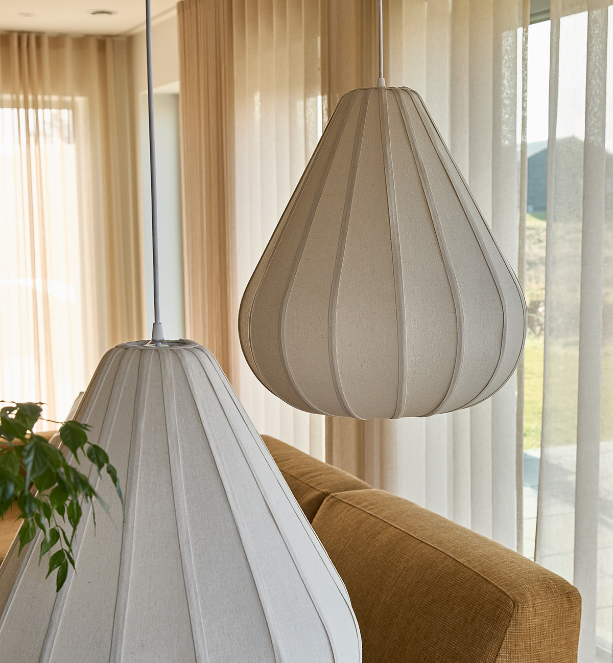 Nærbillede af to beige stofpendler over en sennepsgul sofa i en lys stue med lette gardiner.