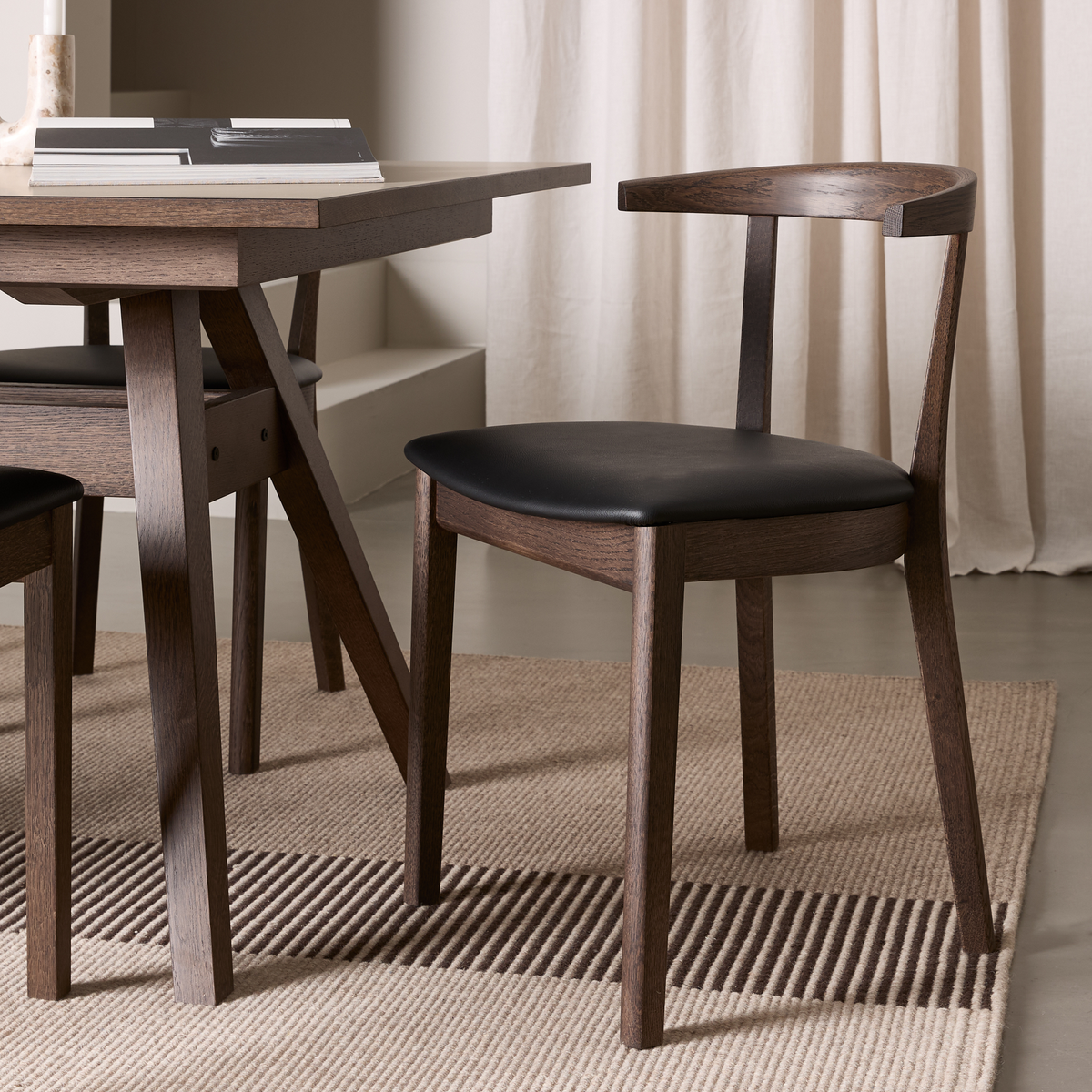 Mørk træspisestol med sort sæde ved siden af et træbord på beige tæppe i et minimalistisk rum.