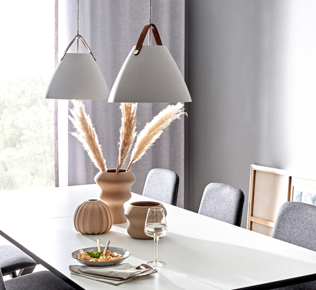 Lyst spisebord med grå stole, to hvide pendellamper med læderstropper og beige vaser med pampasgræs i dagslys.