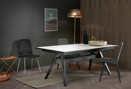 Moderne spiseplads med sort bukbord med hvid bordplade, grå stole, kobberfarvet gulvlampe samt vaser og skål på bordet.