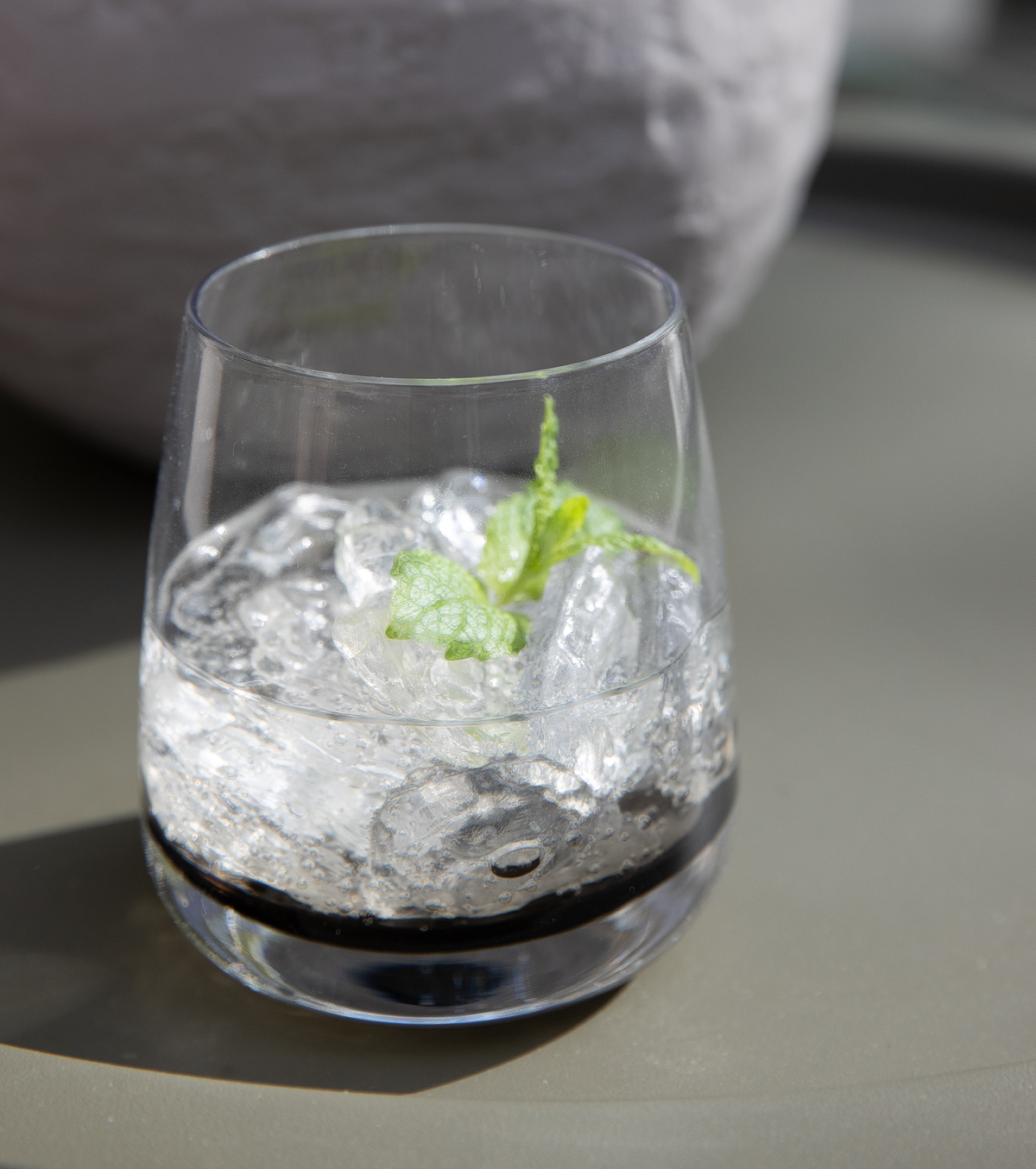 Nærbillede af et glas med knust is, danskvand og en myntekvist på et bord i sollys.