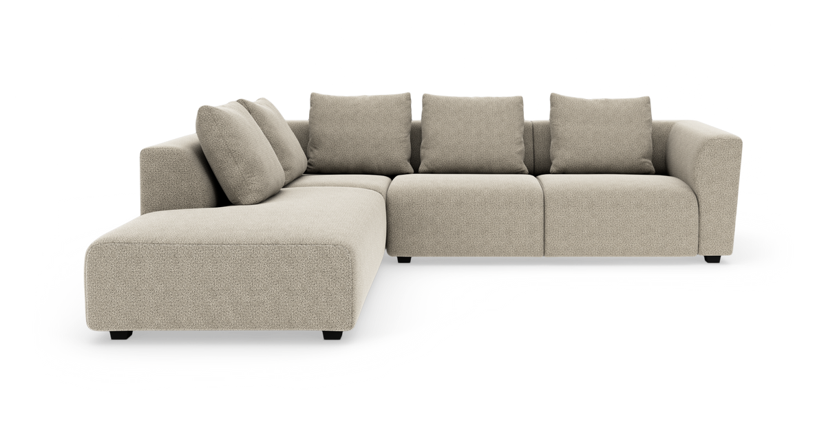 Beige L‑formet modulsofa med chaiselong og fire rygpuder, set forfra i en studieopstilling.