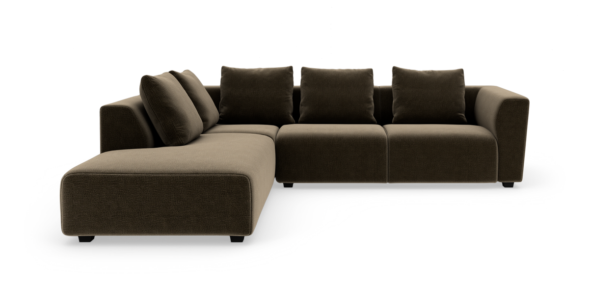 Modulær L‑sofa i mørkebrunt stof med venstrevendt chaiselong og fire rygpuder, moderne lavt design i studielys.