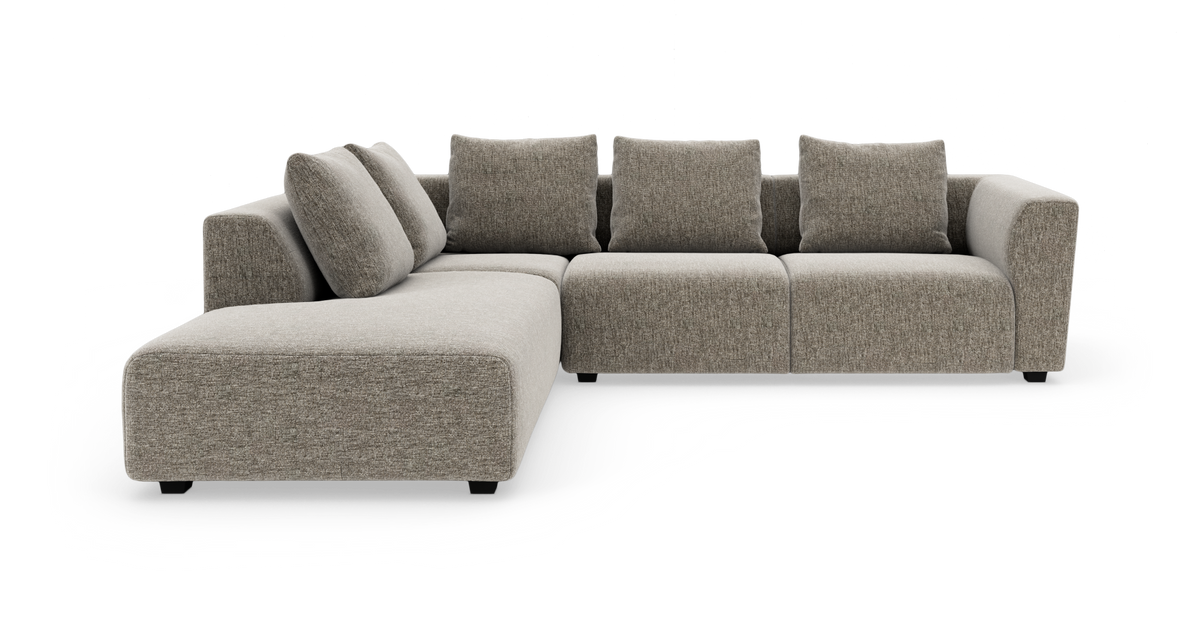 Modulsofa i L‑form med bred chaiselong til venstre, polstret i lysegrå/beige stof med løse ryghynder.