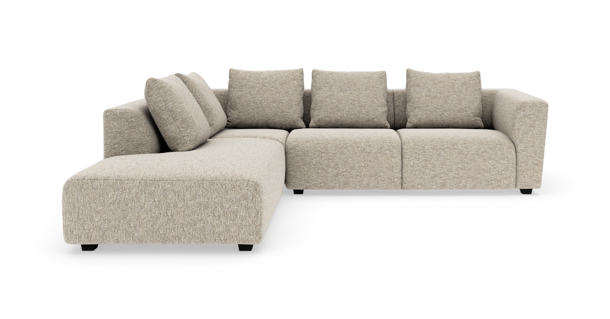 Beige modulsofa i L‑form med bred chaiselong og løse rygpuder.