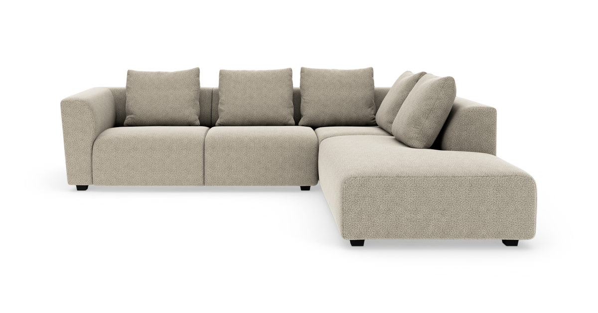 Beige modulsofa i L-form med højre chaiselong, fire ryghynder og blødt afrundede armlæn på hvid baggrund.