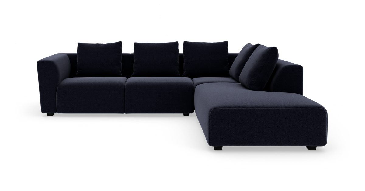 Modulær L‑sofa i mørk marineblåt stof med højrevendt chaiselong og fem løse rygpuder, fritlagt på hvid baggrund.