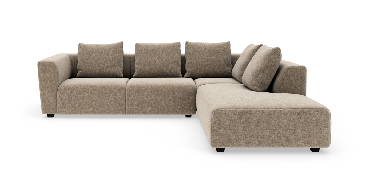 Beige L‑formet modulsofa med chaiselong til højre og fire ryghynder, fritstående på hvid baggrund.