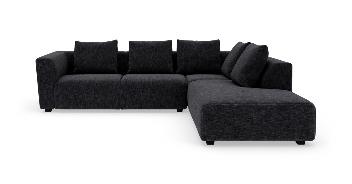 Mørkegrå modulsofa i stof med chaiselong på højre side, frilagt på hvid baggrund.