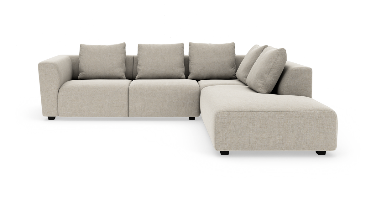 Beige modulsofa med chaiselong til højre og fire ryghynder, frilagt på hvid baggrund.