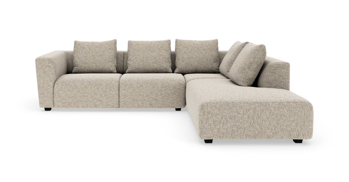 Beige modulsofa i L-form med chaiselong til højre og fire ryghynder, frilagt på hvid baggrund.