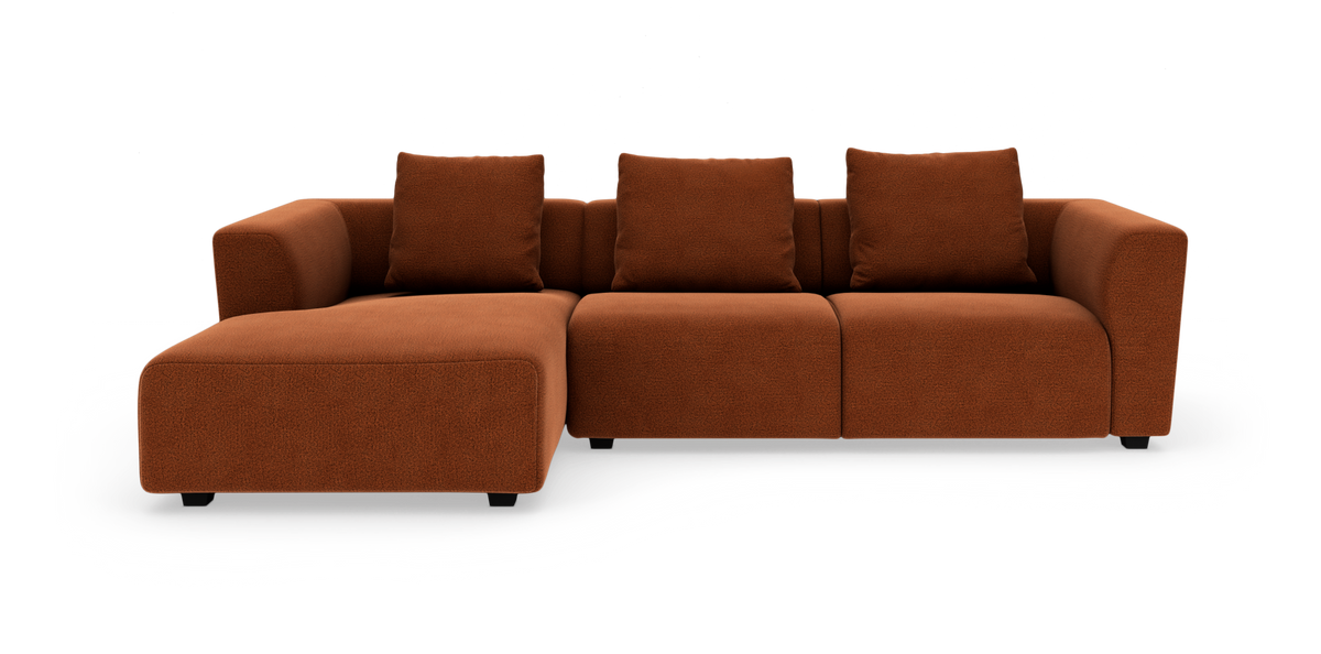 Rustfarvet modulsofa med venstrevendt chaiselong, tre sæder og fire puder, frilagt på hvid baggrund.