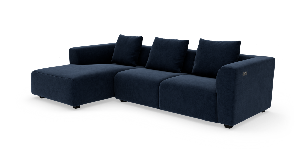 Mørkeblå modulsofa i velour med venstrevendt chaiselong og fire ryghynder på hvid baggrund.