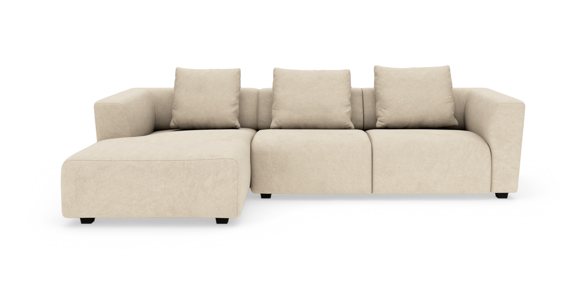 Beige modulsofa med chaiselong til venstre og fire rygpuder, frilagt på hvid baggrund.