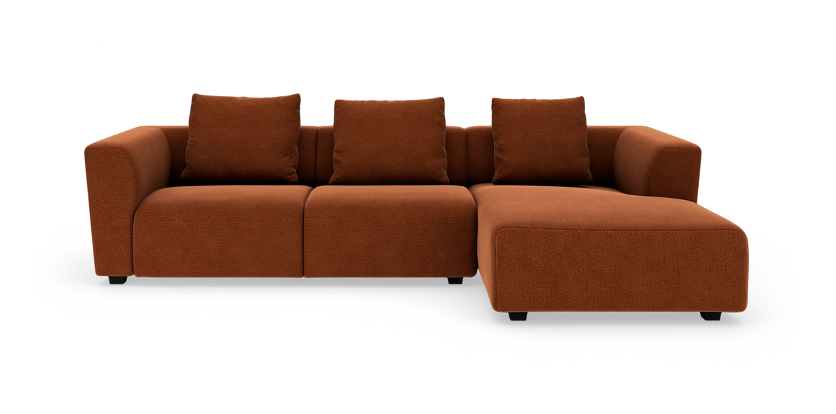 Modulsofa i rustbrunt stof med chaiselong til højre og tre løse ryghynder.