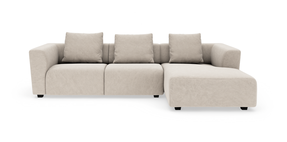 Beige modulsofa i L-form med chaiselong til højre, set forfra mod hvid baggrund.