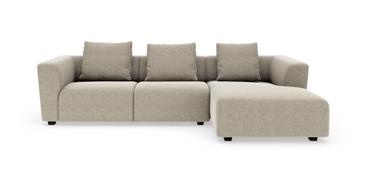 Beige modulsofa med chaiselong til højre, tre sæder og fire puder, moderne bløde former på hvid baggrund.