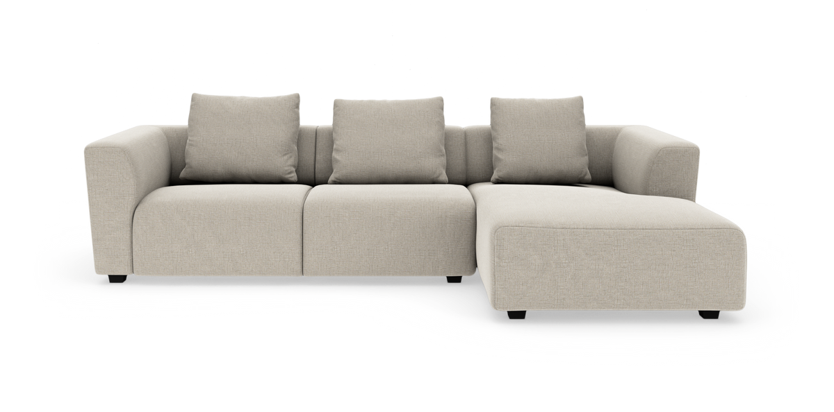 Beige modulsofa med chaiselong til højre, fire rygpuder og afrundede armlæn, frilagt på hvid baggrund.
